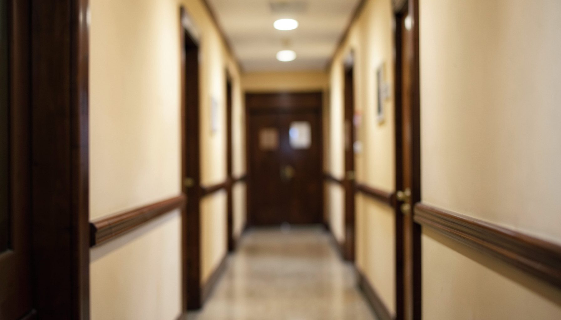 A softly lit academic hallway with warm cream walls and dark wood trim, seen through a shallow depth of field that creates a calm, scholarly atmosphere.