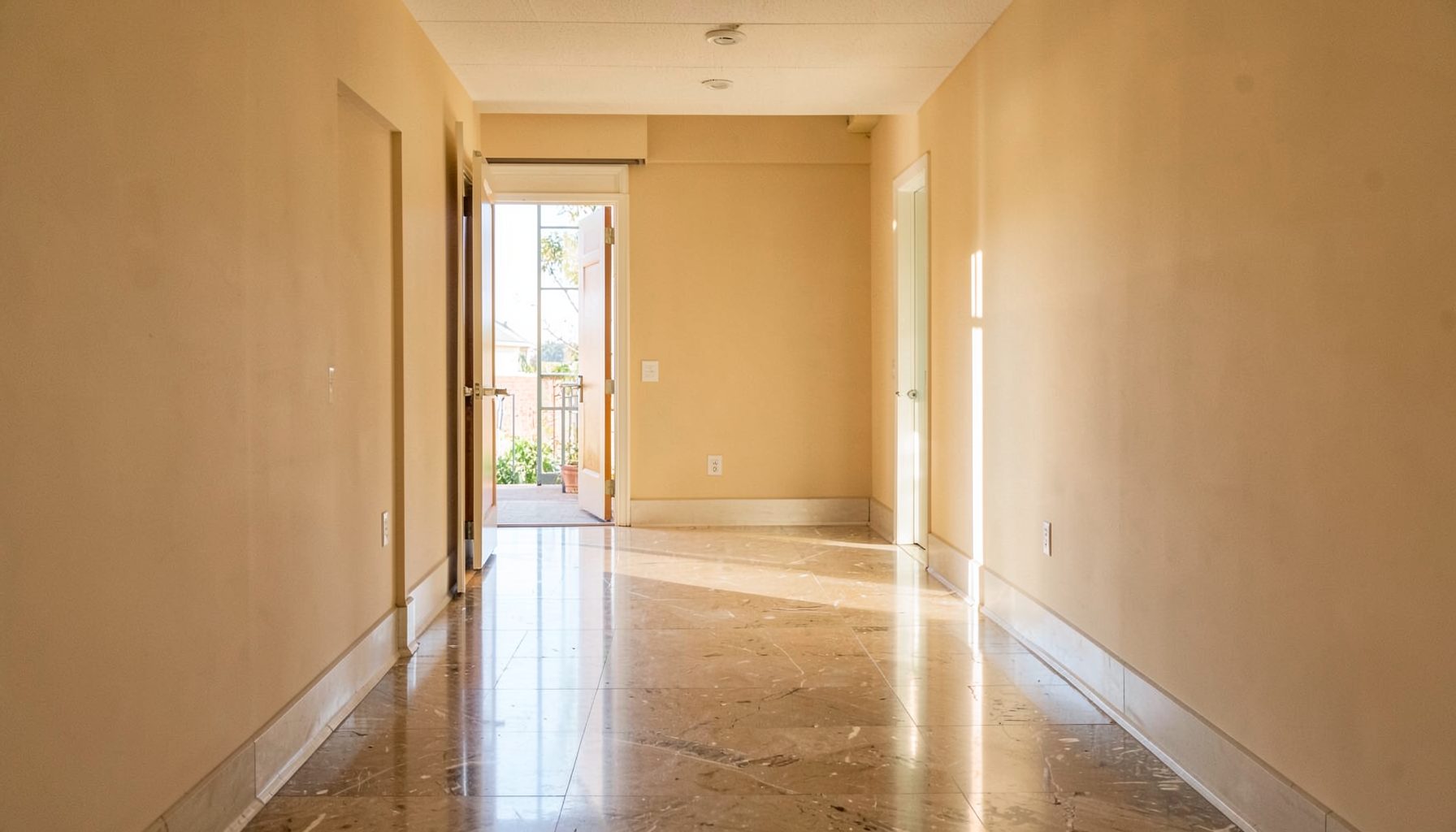 Sunlit college corridor with warm beige walls and polished stone floors, leading toward an open doorway, calm and welcoming